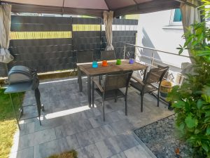 Zu sehen ist eine Terrasse mit Gartenmöbeln und Grill.